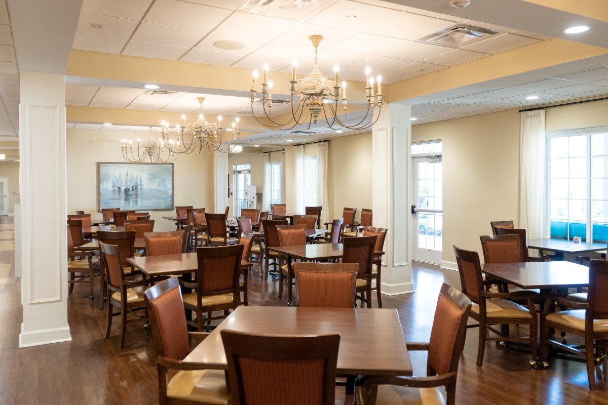 An elegant dining room with multiple tables and chairs, adorned with chandeliers.