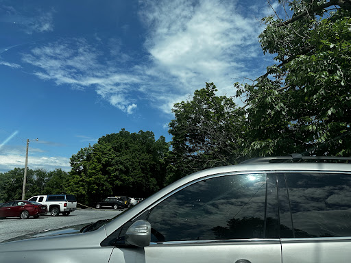 A silver car parked under a blue sky with fluffy clouds and green trees.