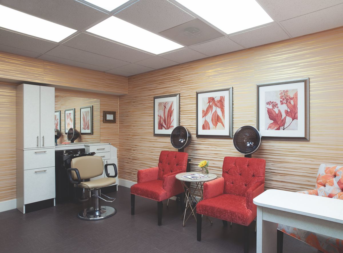 A cozy salon interior featuring red chairs, hair dryers, artwork on the walls, and mirrors under bright lighting.