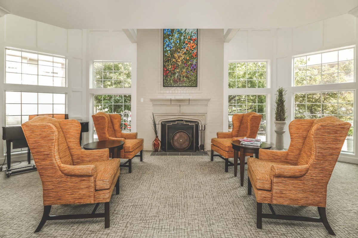 A cozy living room with orange armchairs arranged around a fireplace, complemented by a decorative painting above.