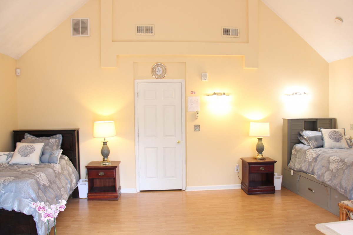 A spacious bedroom with two nightstands and lamps, featuring a central door and wooden flooring.