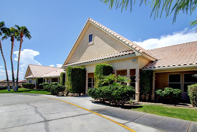 A sunny view of a residential building with well-maintained landscaping and a driveway.