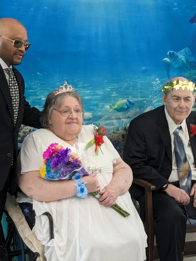A joyful wedding celebration featuring a couple in formal attire, adorned with floral accessories and surrounded by an underwater-themed backdrop.