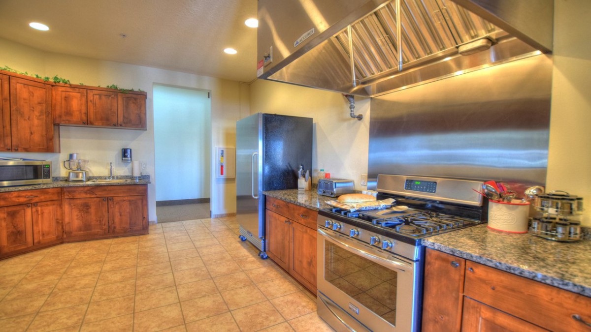 A modern kitchen featuring stainless steel appliances and a large gas stove with wooden cabinets and tile flooring.