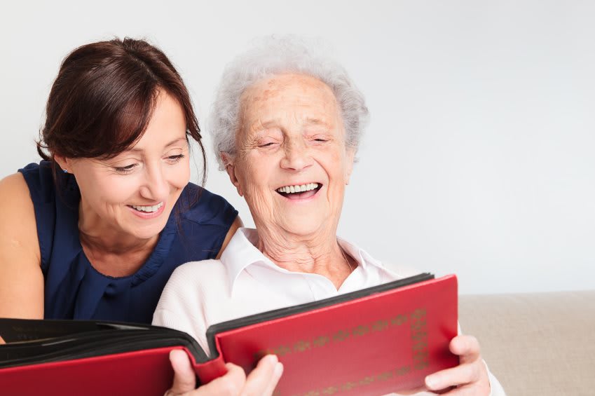 An elderly person and a caregiver enjoying a book together, sharing smiles and warmth.