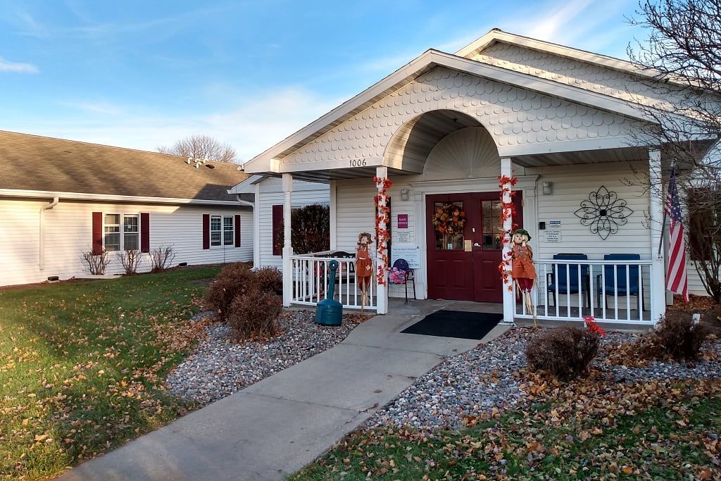 A charming house with seasonal decorations on the front porch surrounded by autumn leaves.