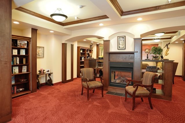 A cozy lounge area with carpeted flooring, comfortable chairs, and a fireplace.