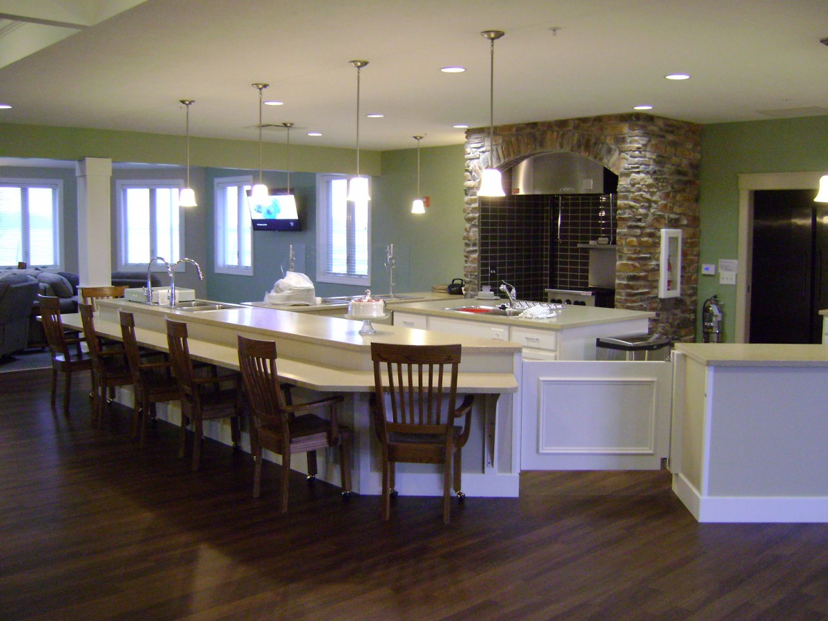 A modern kitchen with a large bar counter, pendant lighting, and wooden flooring.