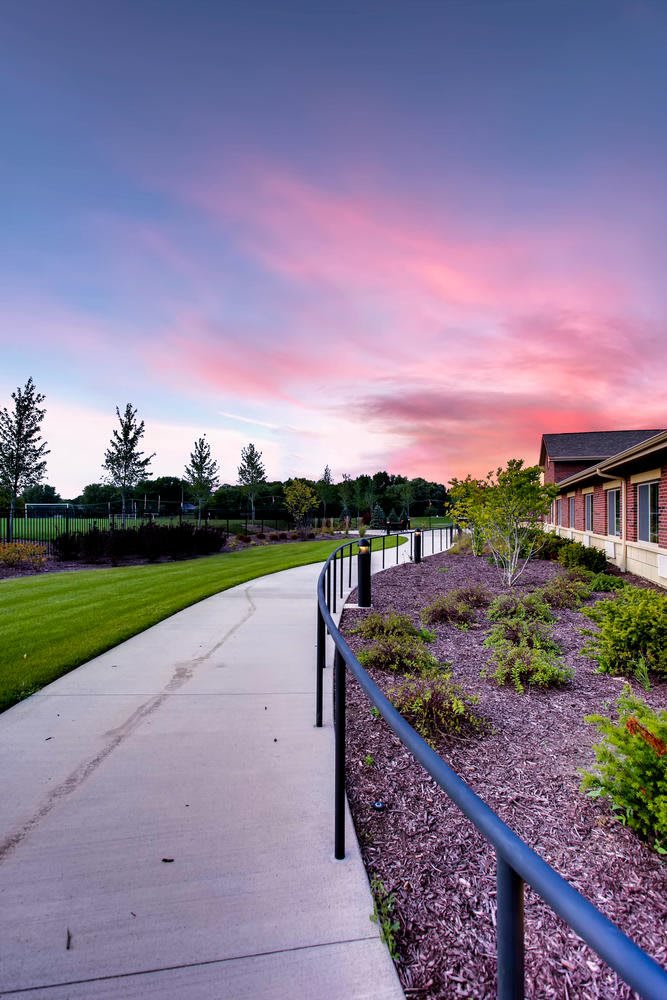 A scenic pathway beside a building at sunset, surrounded by a well-maintained garden and lush trees.