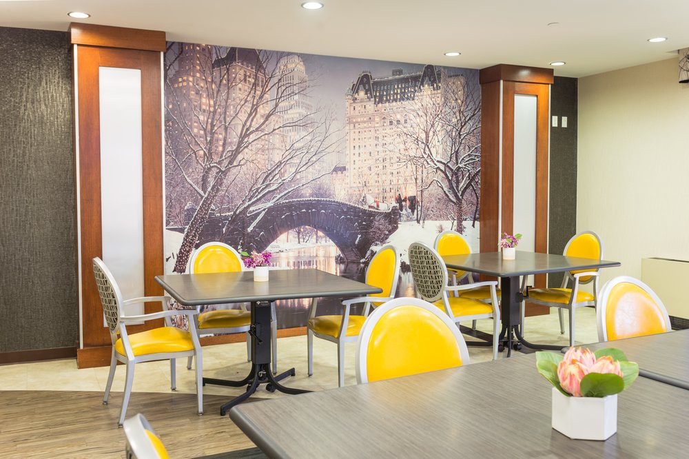 A cozy cafe interior featuring yellow chairs and a large mural of a winter cityscape.