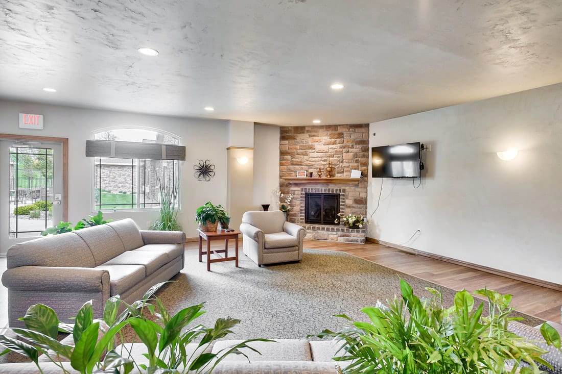 A cozy living room with a stone fireplace, comfortable seating, and houseplants.