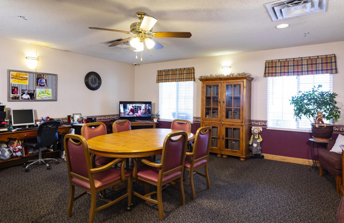 A dining room features a round table with chairs, a wooden cabinet, and a television.