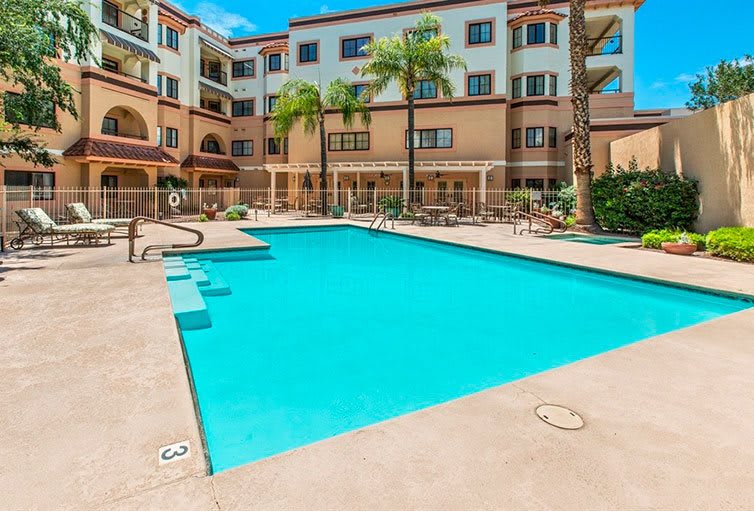 A modern apartment complex with an outdoor swimming pool surrounded by palm trees.