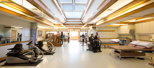 A well-lit rehabilitation center featuring various therapy equipment and patients engaging in physical therapy sessions.