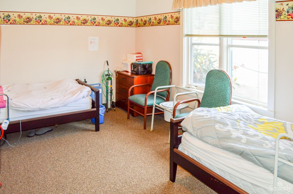 A shared room in a nursing home with two hospital beds, chairs, and medical equipment.