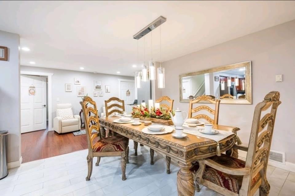 An elegant dining room featuring a wooden table with intricate carvings, surrounded by matching chairs. The table is set for a meal, and decorative lighting hangs above, enhancing the sophisticated ambiance.