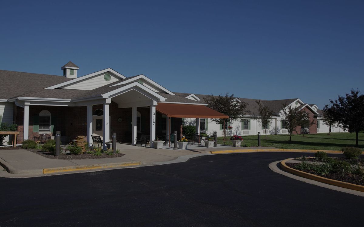 A view of a building entrance with a covered area and landscaped surroundings on a sunny day.