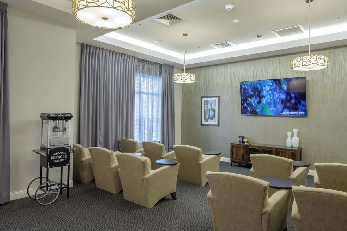 A well-lit waiting room with comfortable chairs, a large TV, and elegant curtains.