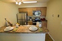 A modern kitchen featuring wooden cabinets, stainless steel appliances, and a small dining area.