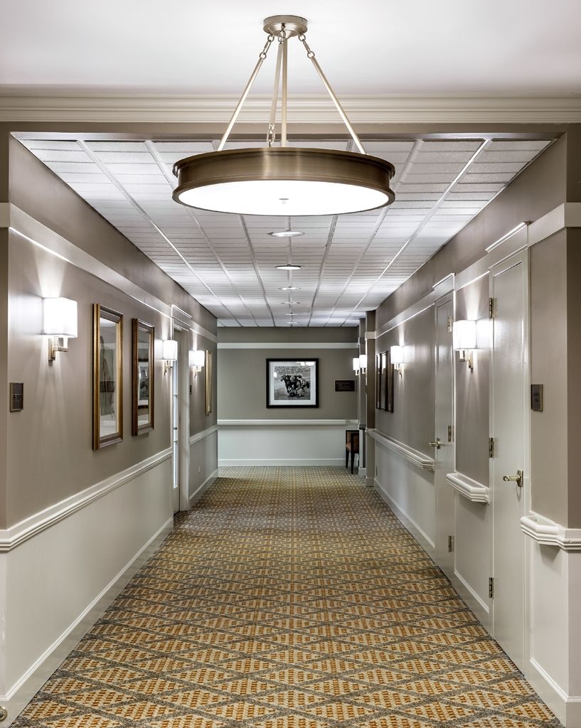 A well-lit hotel hallway with framed artwork and patterned carpet.