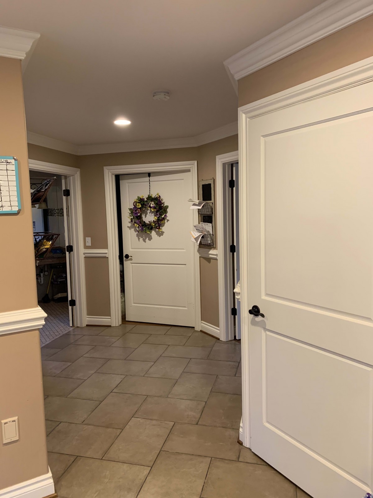 A cozy home hallway with beige walls and multiple doors, featuring a wreath on the central door.