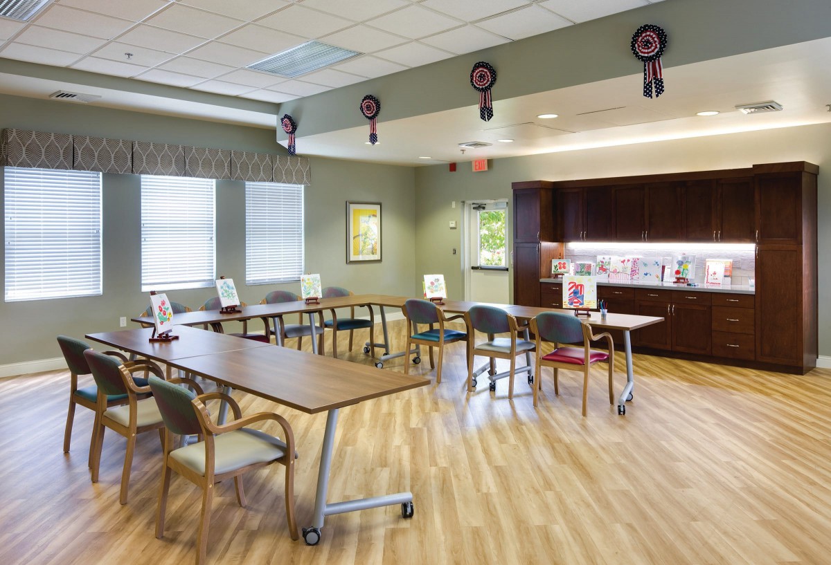A well-lit classroom with multiple tables and chairs, featuring a wooden floor and wall decorations.