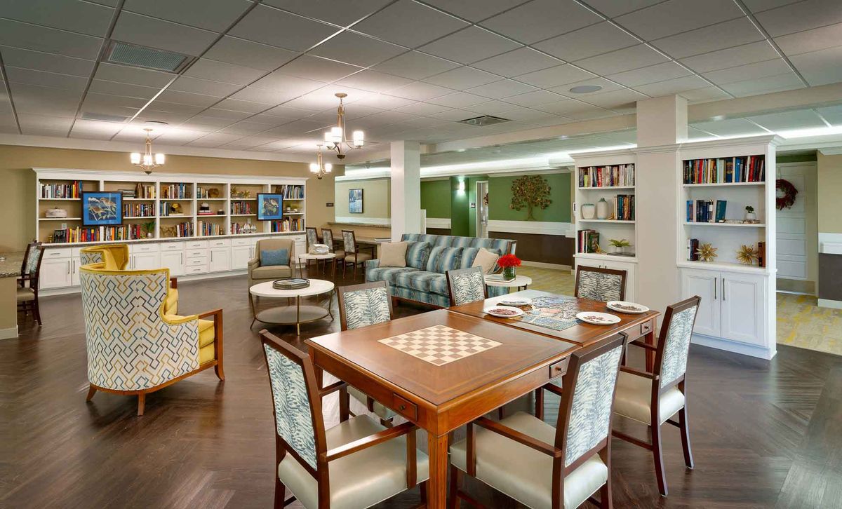 A cozy and well-furnished lounge area featuring a chess table, comfortable seating, and bookshelves with ample lighting.