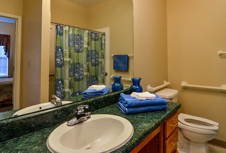 A well-organized bathroom with a green and blue color scheme, featuring a sink, mirror, neatly folded towels, and a decorative shower curtain.