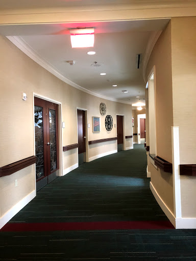 A view of a well-lit hallway with carpeted floors and doors along the sides.