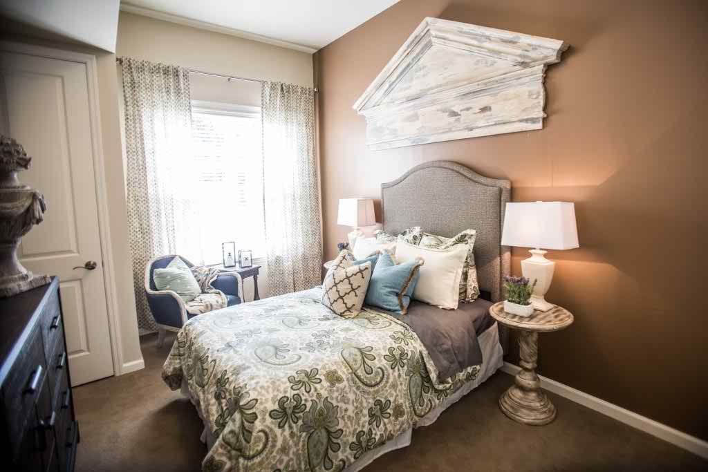 A cozy bedroom with elegant decor, featuring a bed adorned with patterned bedding and pillows, flanked by lamps on nightstands near a bright window.