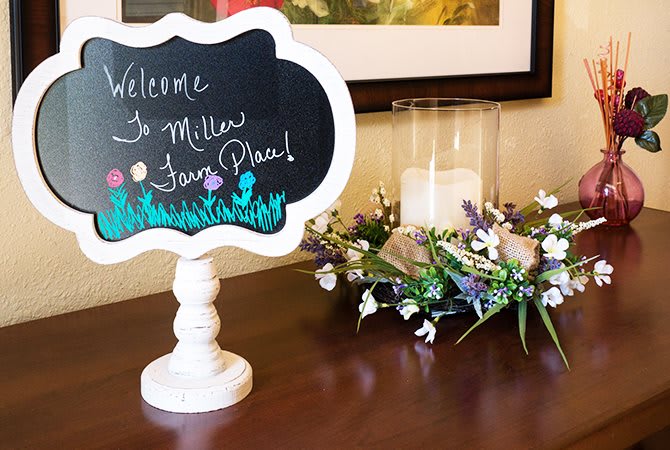 A welcoming setup featuring a blackboard sign, decorative flowers, and a candle.