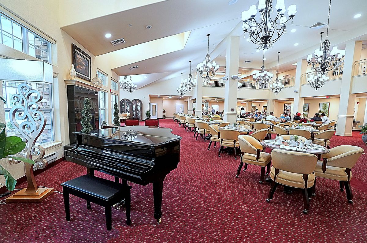 A spacious and elegant dining area features a grand piano, plush chairs, and ornate chandeliers.