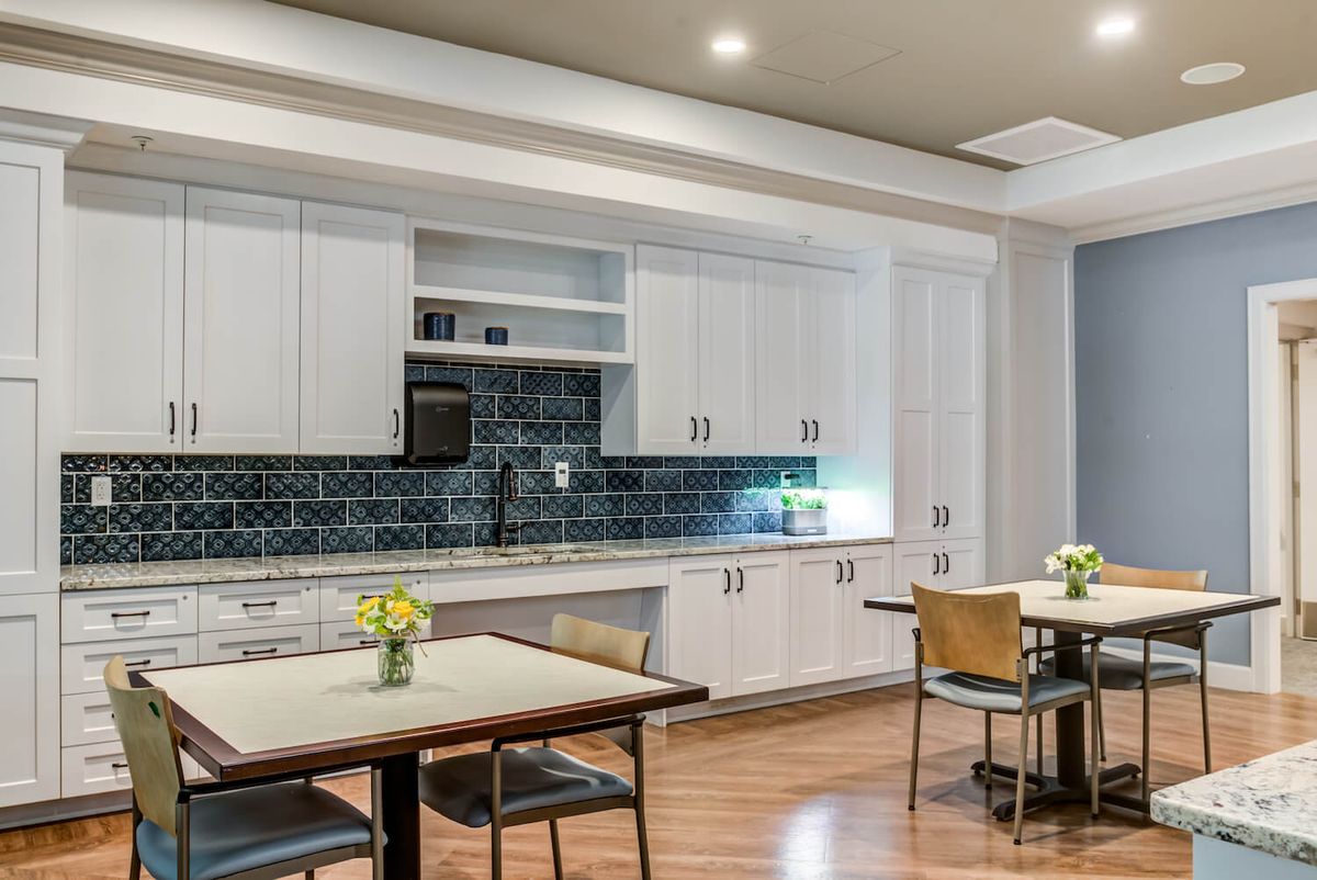 A modern kitchen and dining area with white cabinets, a black backsplash, and wood flooring.