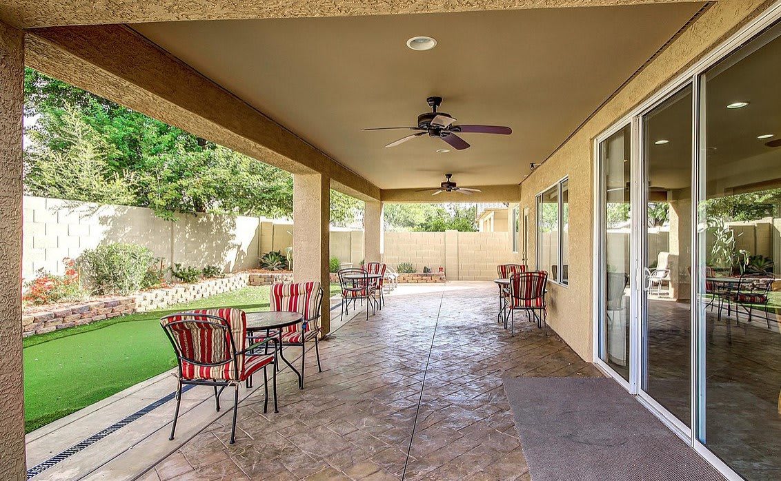 A covered patio with outdoor seating and ceiling fans overlooking a garden.