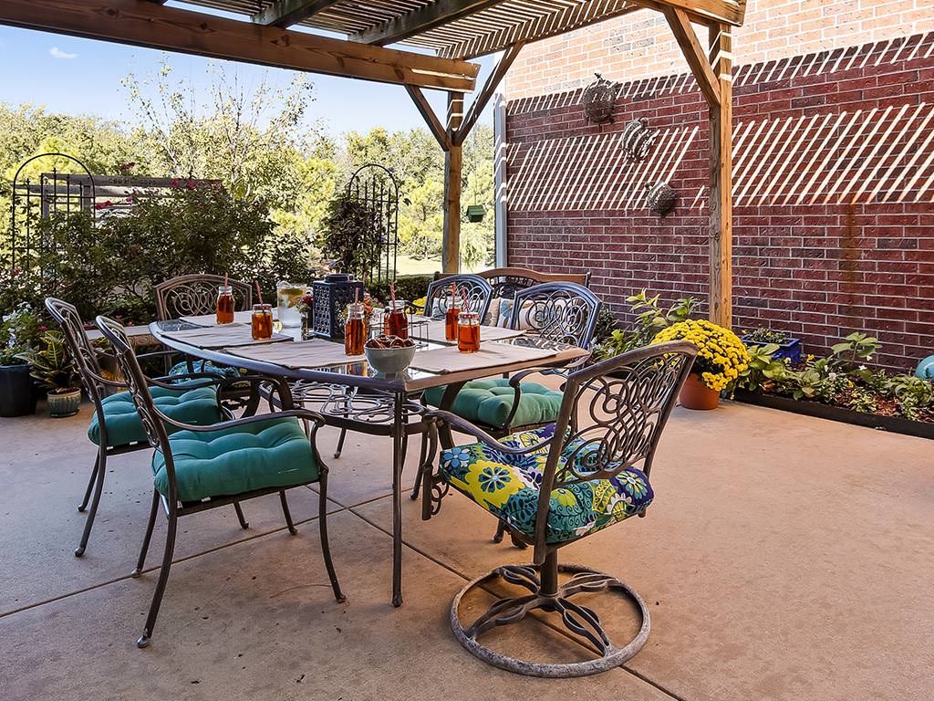 A cozy outdoor patio with a table and chairs under a pergola, surrounded by potted plants.