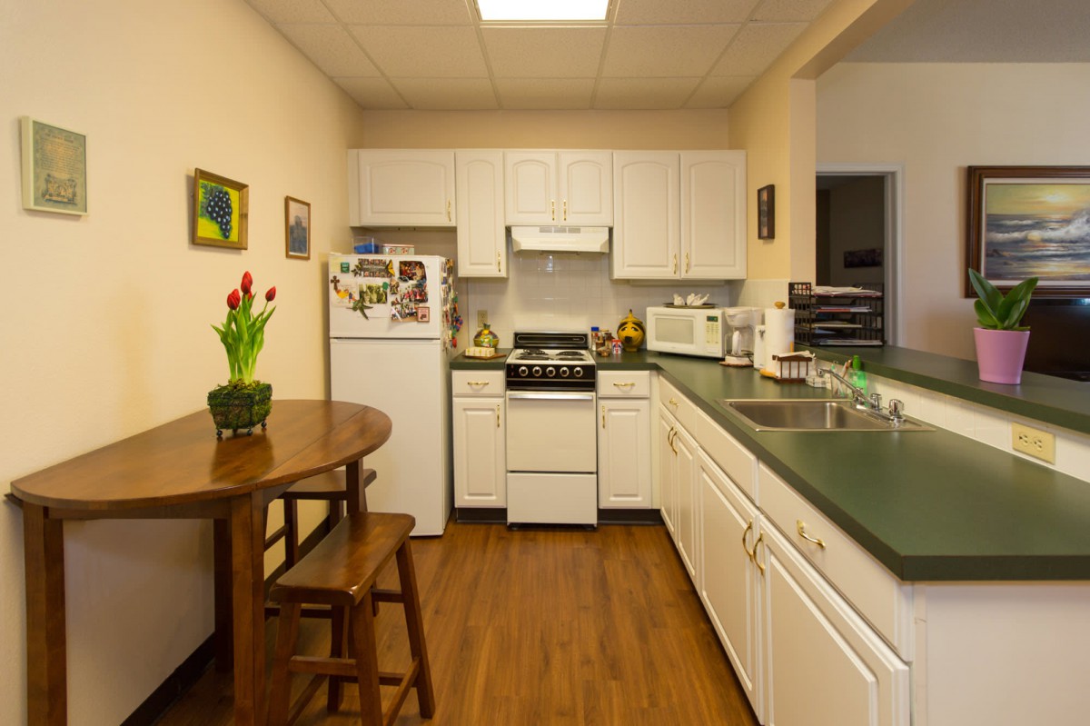 A cozy kitchen with white cabinets, featuring modern appliances and a small dining area with flowers on the table.