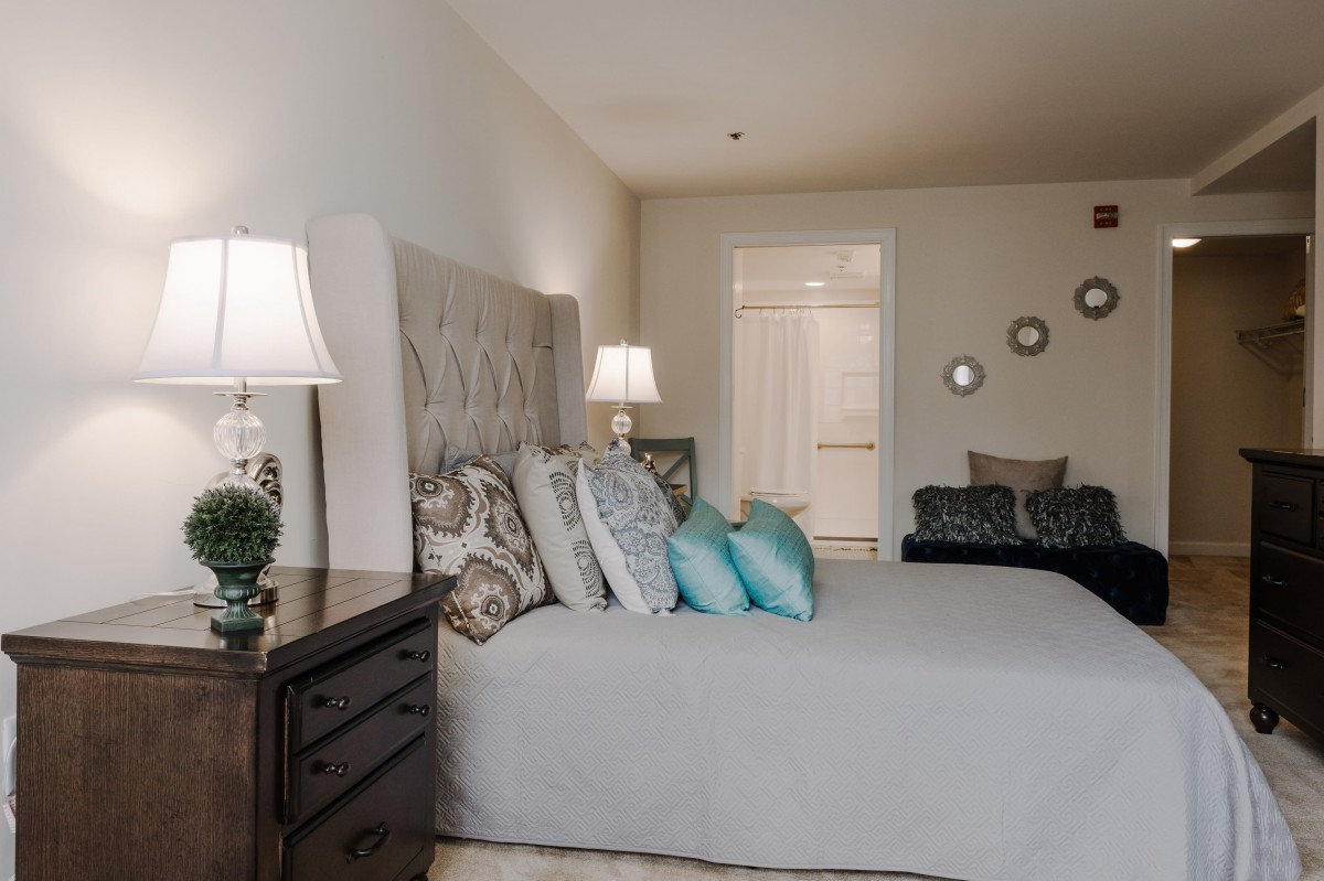 A cozy bedroom interior with a neatly made bed, decorative pillows, and ambient lighting.