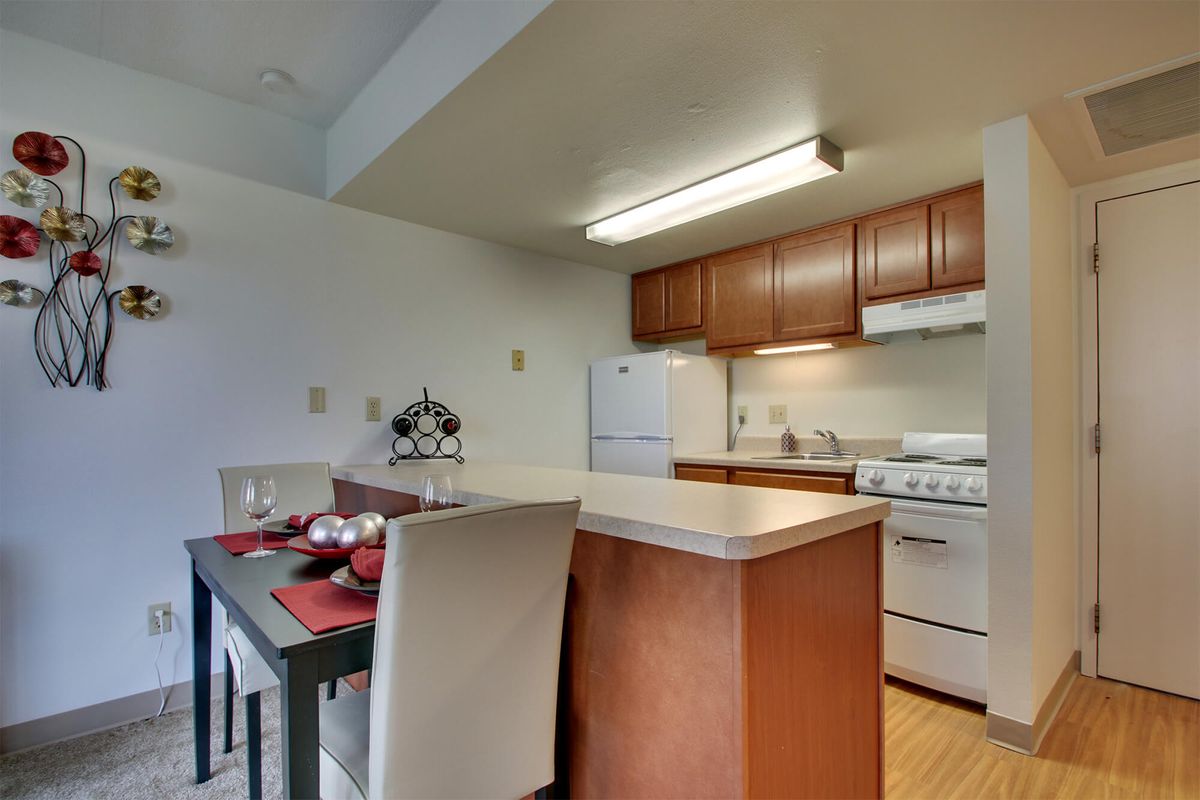 A modern kitchen and dining area in an apartment with wooden cabinets, a stove, and refrigerator.