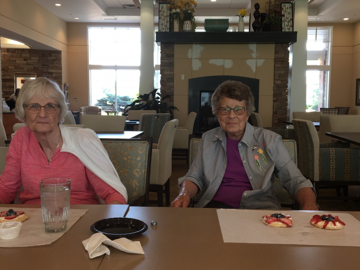 Two seniors seated at a table, enjoying a meal indoors.