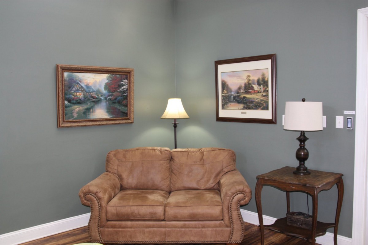 Cozy living room corner with a brown sofa, floor lamp, and framed artwork on the walls.
