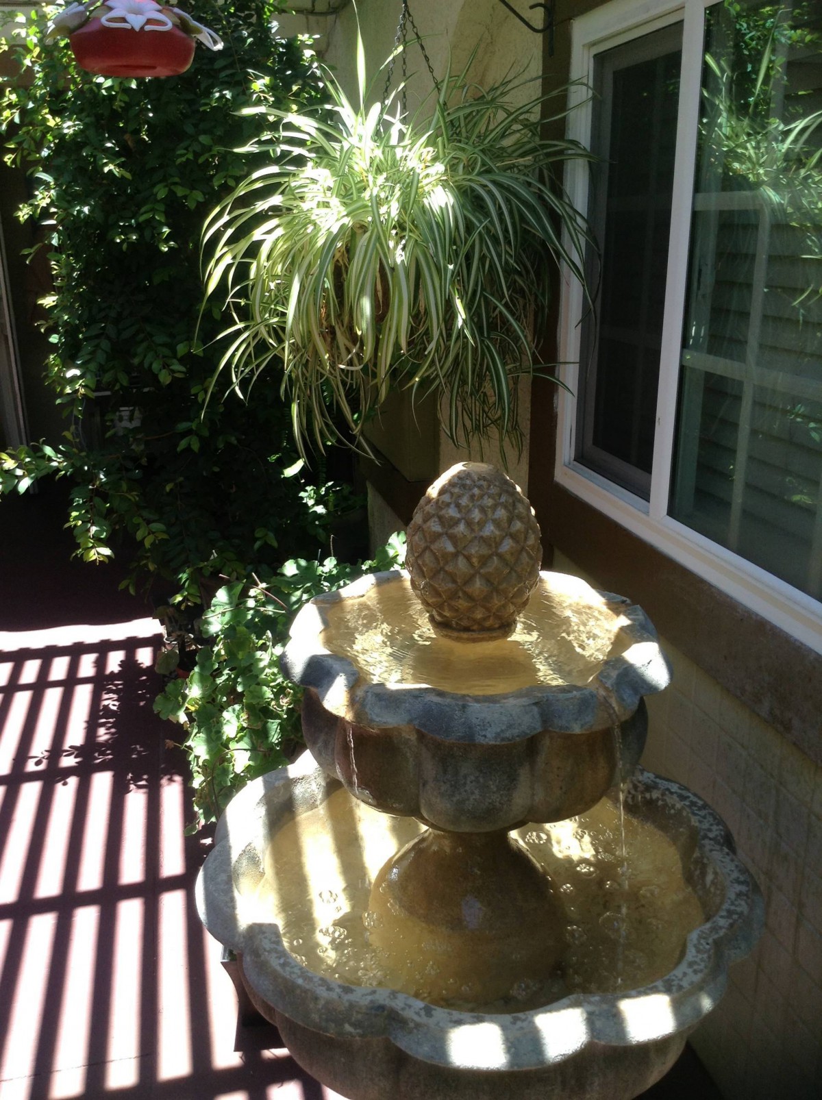 A garden fountain adorned with a pineapple ornament, surrounded by lush greenery and bathed in sunlight.