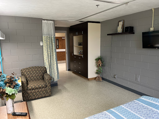 A cozy room featuring a patterned chair, shelving unit, and soft lighting.