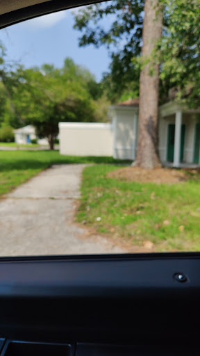 A view of a pathway leading through a grassy area with trees and buildings in the background.