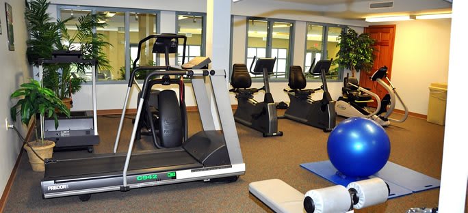 A gym room equipped with treadmills, stationary bikes, and exercise mats.