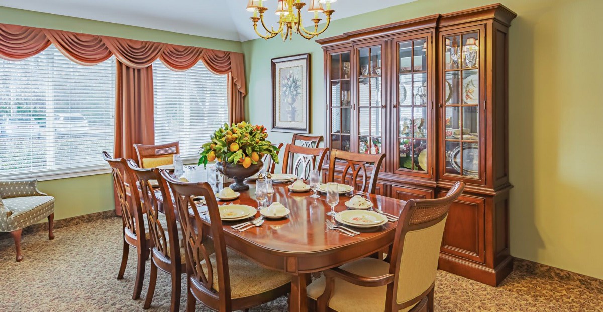 A traditional dining room with a wooden table set for a meal, surrounded by matching chairs and accented by a chandelier overhead.