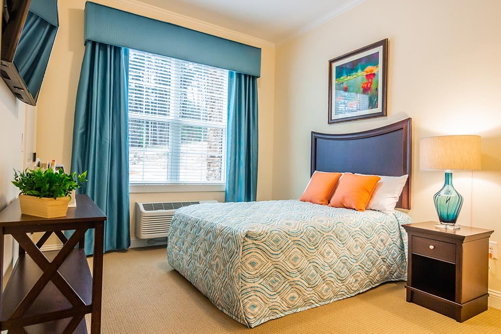 A cozy bedroom with a bed, colorful pillows, and a large window with blue curtains.