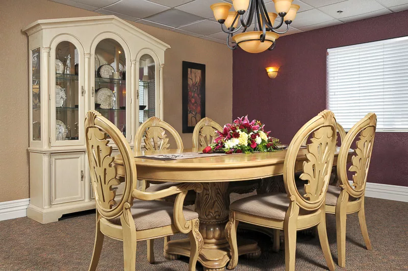 A classic dining room with an ornate round table and matching chairs, accompanied by a china cabinet and elegant chandelier.