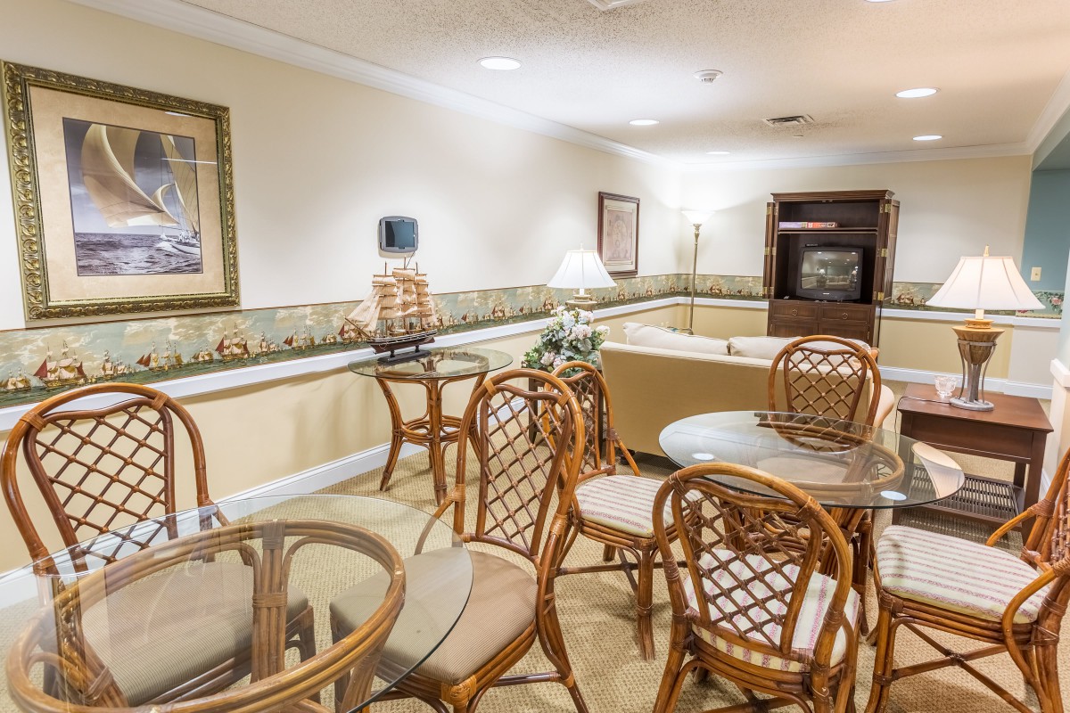 A cozy indoor seating area with wooden tables and chairs, softly lit by a lamp.