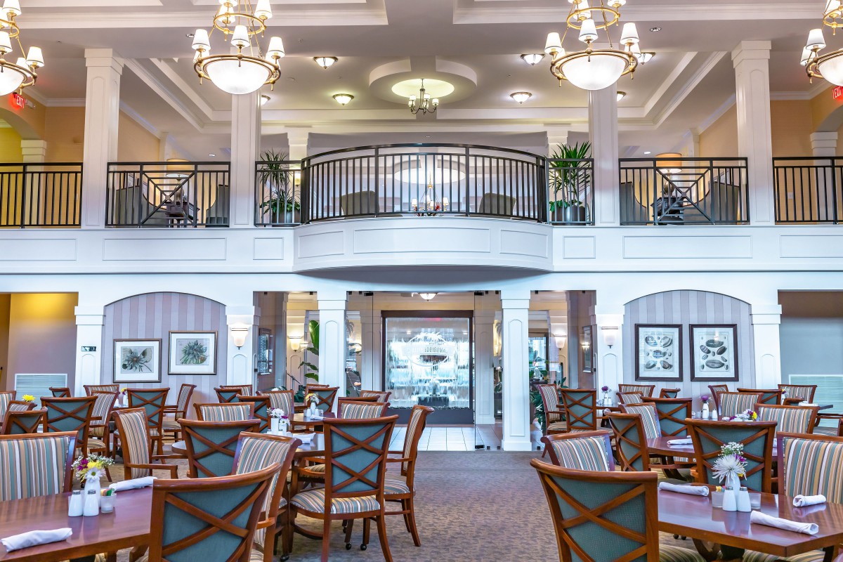 A spacious and elegant dining room with chandeliers, tables, and a balcony.
