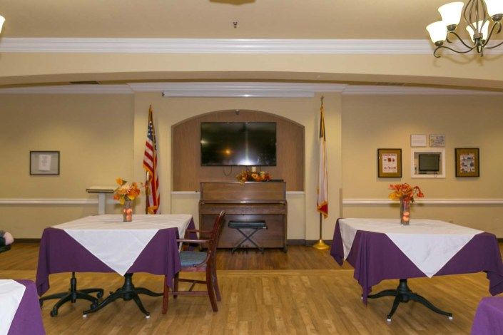 A cozy dining area with tables and chairs, decorated with flowers and flags, featuring a television on the wall.